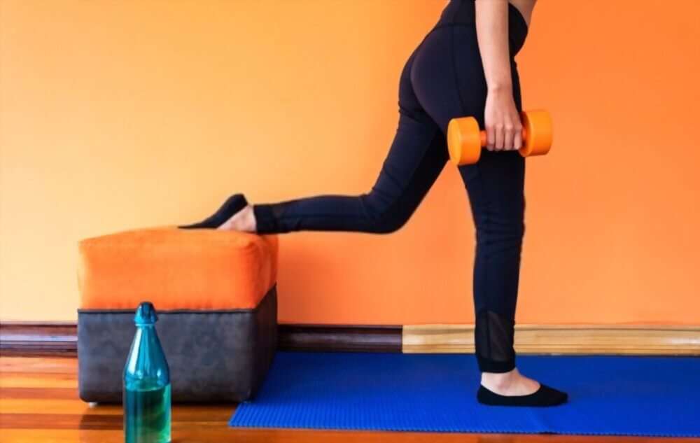 Young woman doing a Bulgarian split squat jump with orange dumbbells